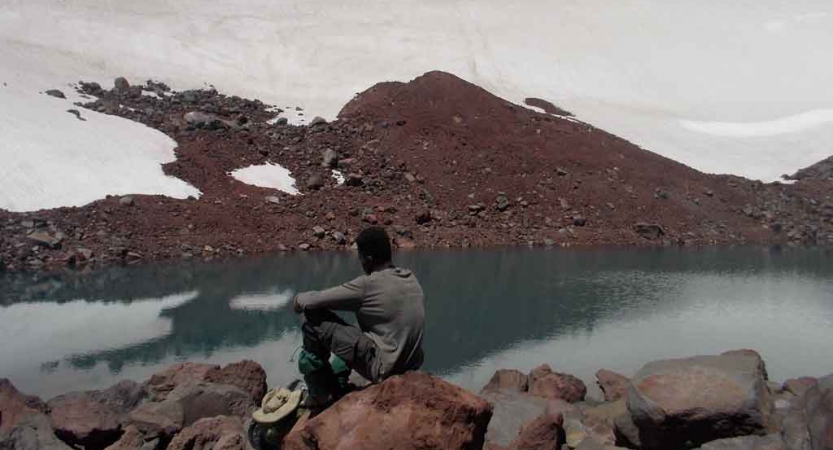 a teen sits near snow and water on backpacking trip 